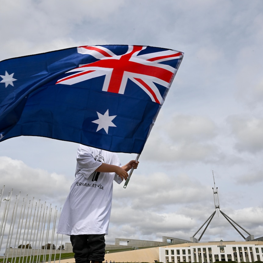 young boy ways the Australian flag on the grassy hill of parliament house