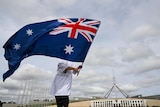 young boy ways the Australian flag on the grassy hill of parliament house