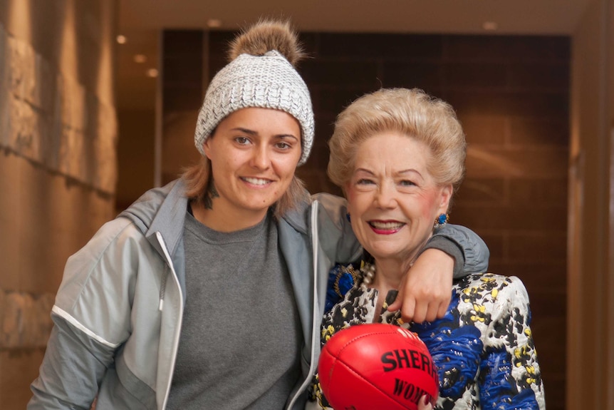Moana Hope stands next to Susan Alberti, who holds a Sherrin football.