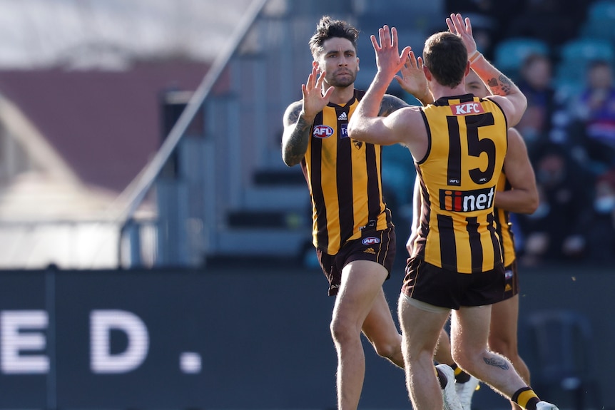 An AFL goalscorer runs past and raises his hands to give a double high-five to a teammate.