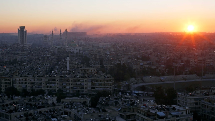 The sun rises while smoke is pictured near Aleppo's historic citadel.