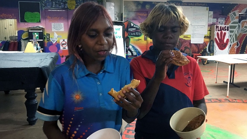 Two Indigenous children eat toast out of bowls at the youth centre