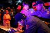 Police lean on the front of a police car while writing notes.