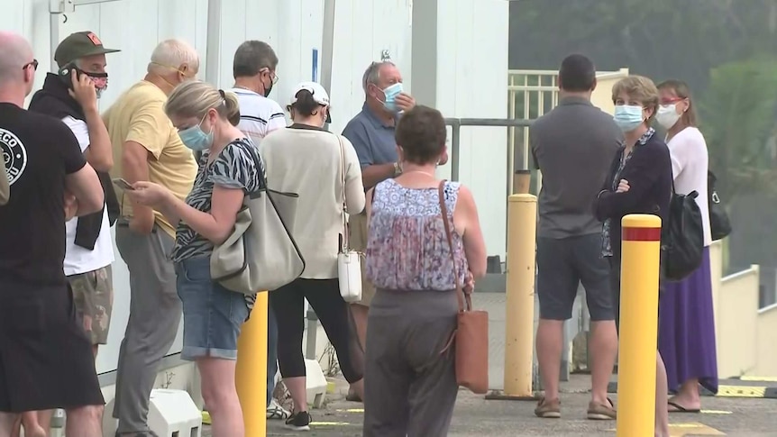 A line of people stand outside a hospital.