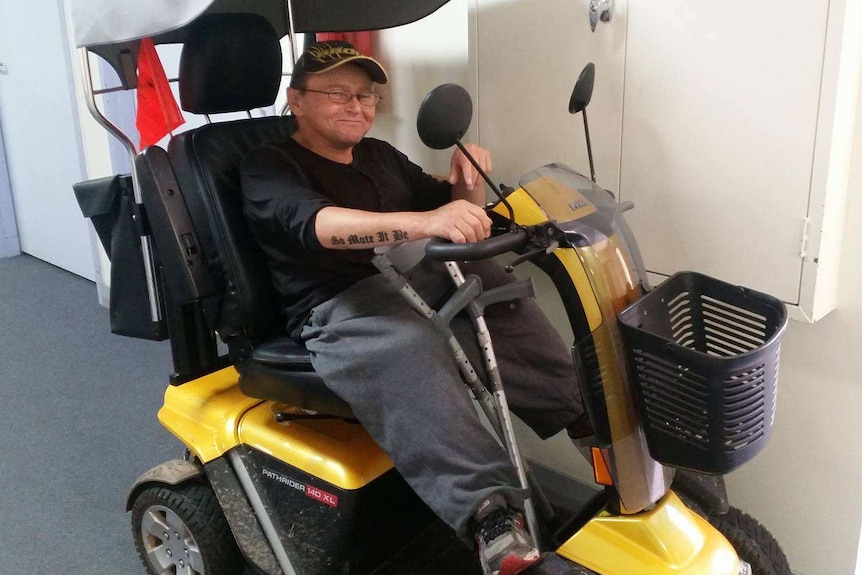 A man with glasses sits in a wheelchair with a an ACDC T-shirt on