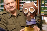 a man dressed in a soldier's outfit holds a brown full face mask built for a small child