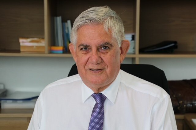 A close up of Ken Wyatt wearing a white shirt and purple tie, looking at the camera in an office.