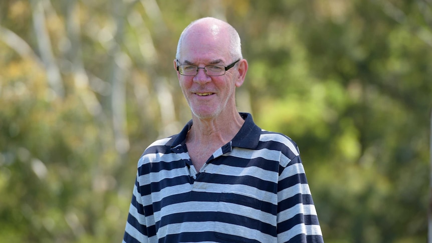 Phil O'Keefe, a man with a striped shirt, smiles at the camera in front of some trees.