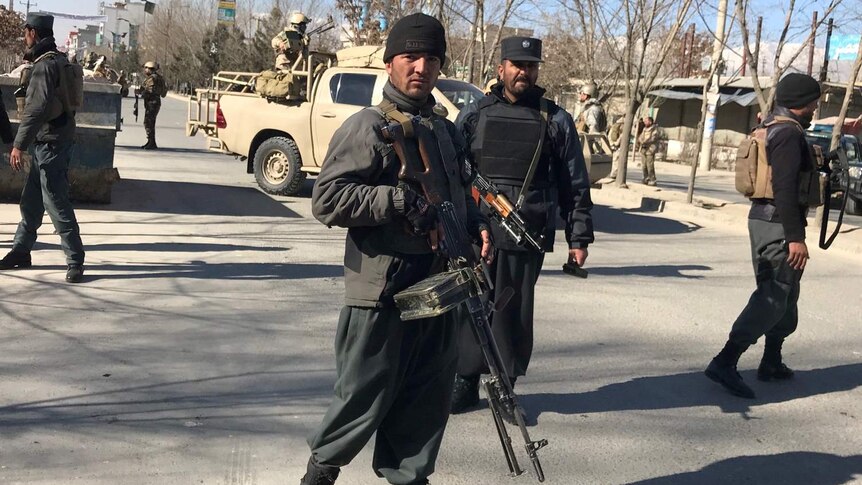 Afghan policemen, one with a large firearm, stand guard on street at the site of a blast in Kabul