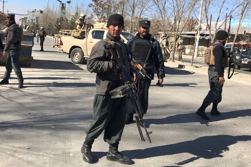 Afghan policemen, one with a large firearm, stand guard on street at the site of a blast in Kabul