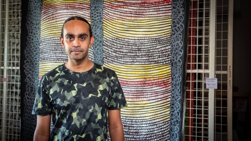 A young man stands in front of a print. 