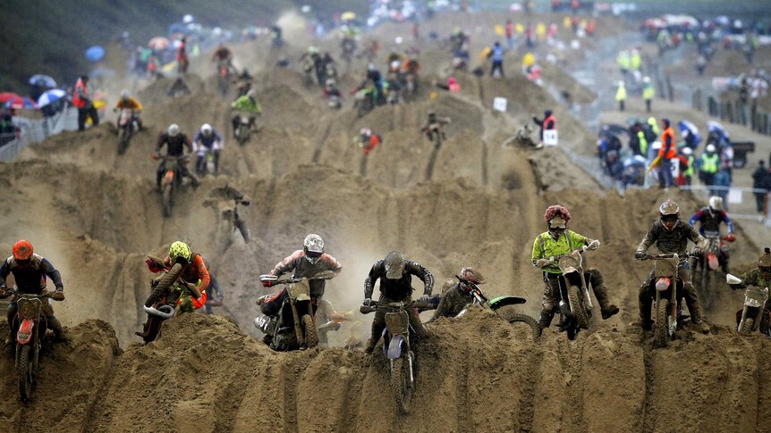 Motorbike riders reach the crest of a dune during a beach race.