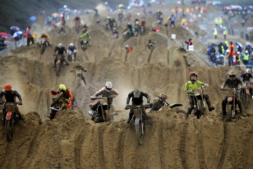 Motorbike riders reach the crest of a dune during a beach race.