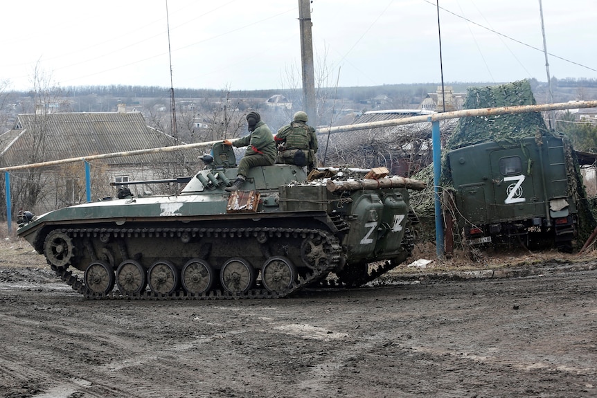 Soldiers sit on top of a Russian tank with Z symbols spray painted on its rear