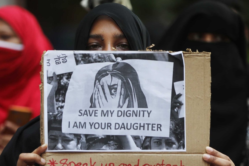 A woman holds up a sign reading "save my dignity, I am your daughter