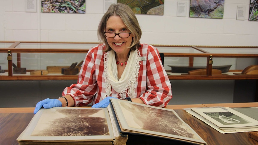 A woman wearing glasses opens an album of historic photographs.