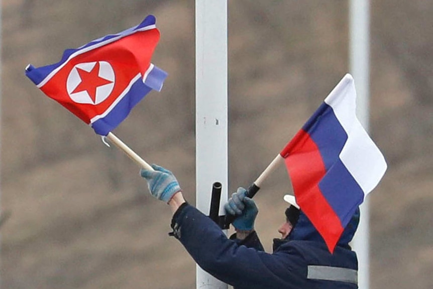 A worker handles the North Korean flag, blue red and white with a star in the middle, and the Russian flag, red, white and blue.