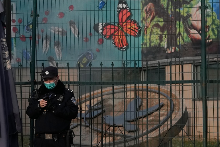 A Chinese police officer stands in front of a large gate and fence