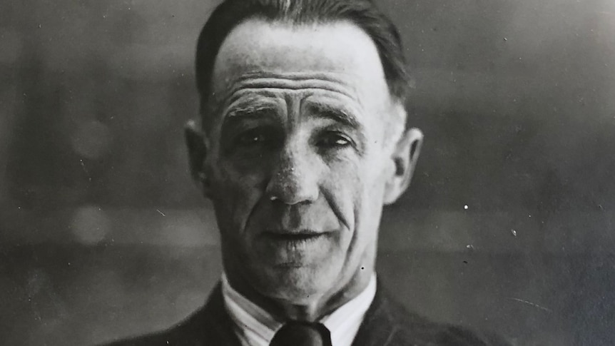 A black and white photo of a middle aged man in suit and tie with slicked back hair.