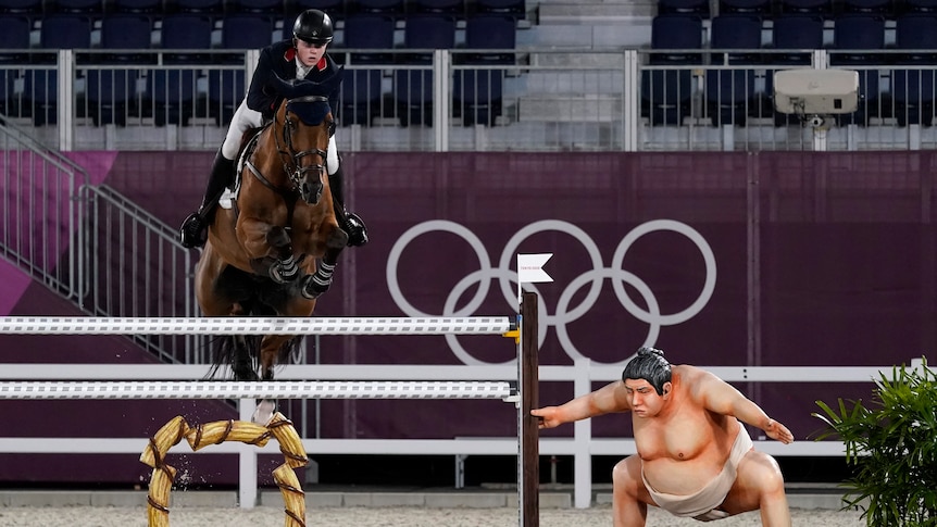 Equestrian jumping over beam next to a statue sumo wrestler at the Tokyo Olympics Games