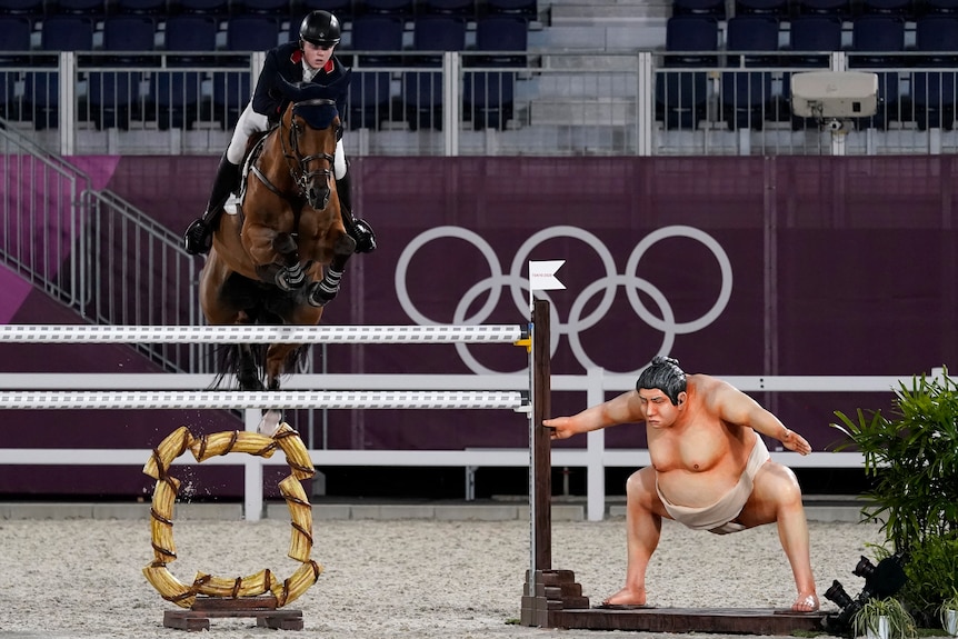 Equestrian jumping over beam next to a statue sumo wrestler at the Tokyo Olympics Games