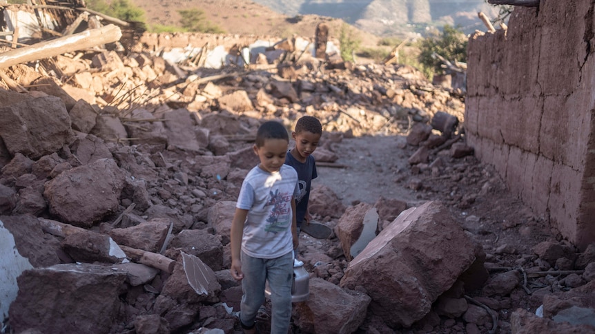 Two boys walk through rubble.