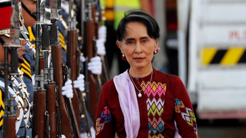 Aung San Suu Kyi walking alongside a row of soldiers holding guns
