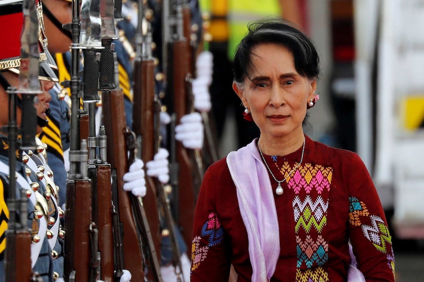 Aung San Suu Kyi walking alongside a row of soldiers holding guns