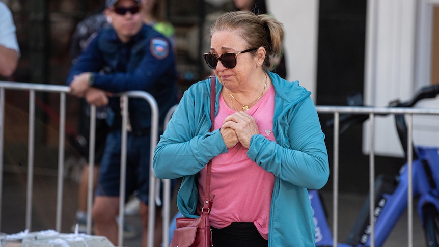 A woman in a tracksuit jacket cries in front of a police barricade at Bondi Junction 