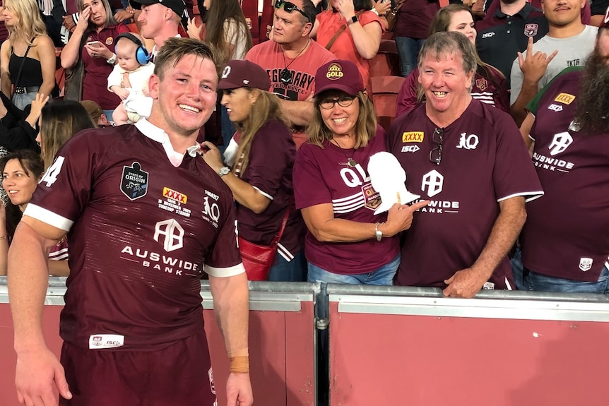 A young man stands in front of two people in a packed stadium