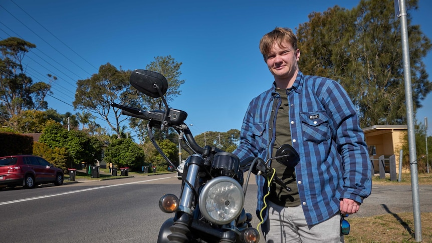 Dion Galea stands smiling at camera, next to a motorcycle.
