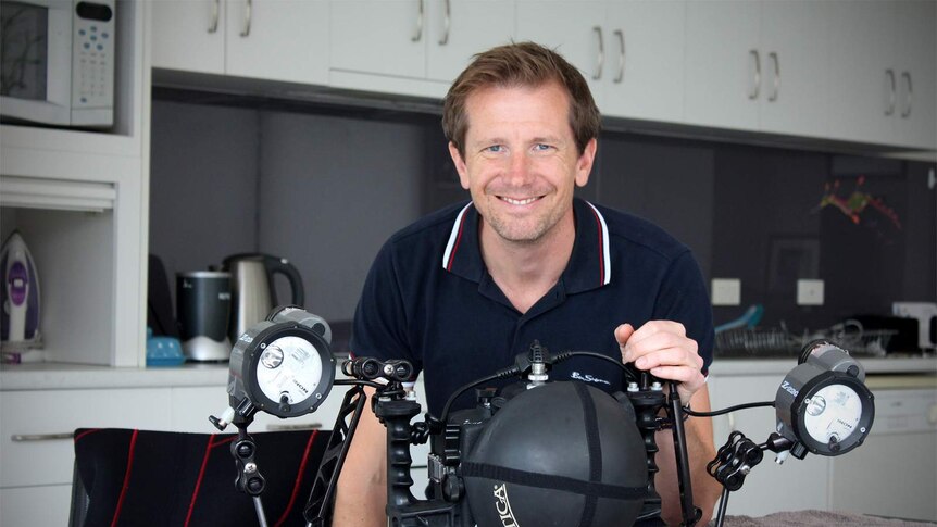 Matt Smith stands in his kitchen holding his under water housing with lights attached.