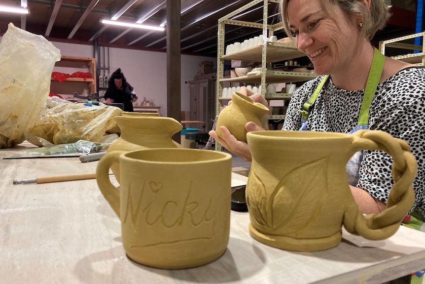 In the foreground is two ceramic mugs, in the background Anna Meares is crafting another mug