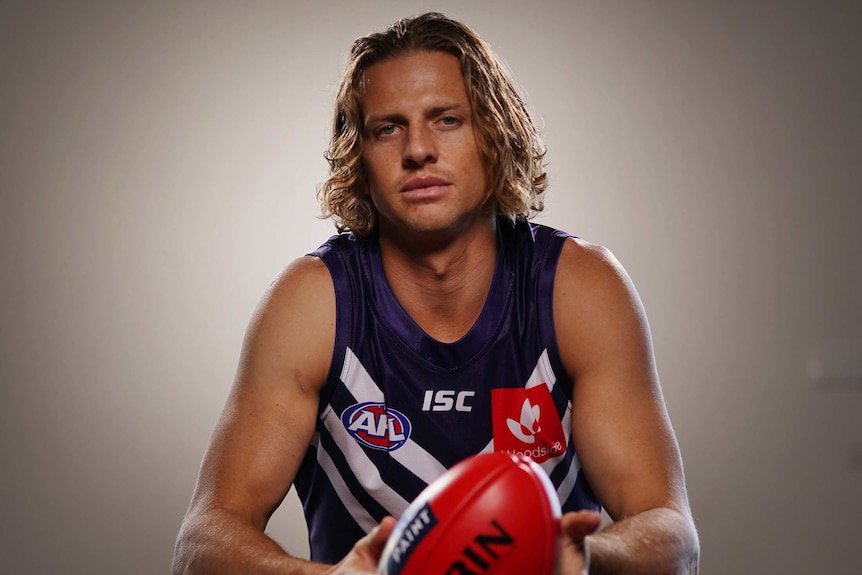 Nat Fyfe sits posing for a photo wearing his Dockers uniform and holding a red football.