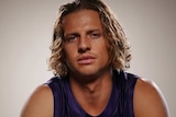 Nat Fyfe sits posing for a photo wearing his Dockers uniform and holding a red football.