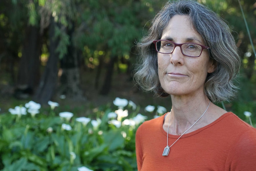 A woman in an orange shirt with glasses in front of arum lilies