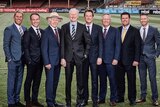 A photo of eight white men dressed in suits from a Wide World of Sports tweet announcing their men's Ashes commentary team.