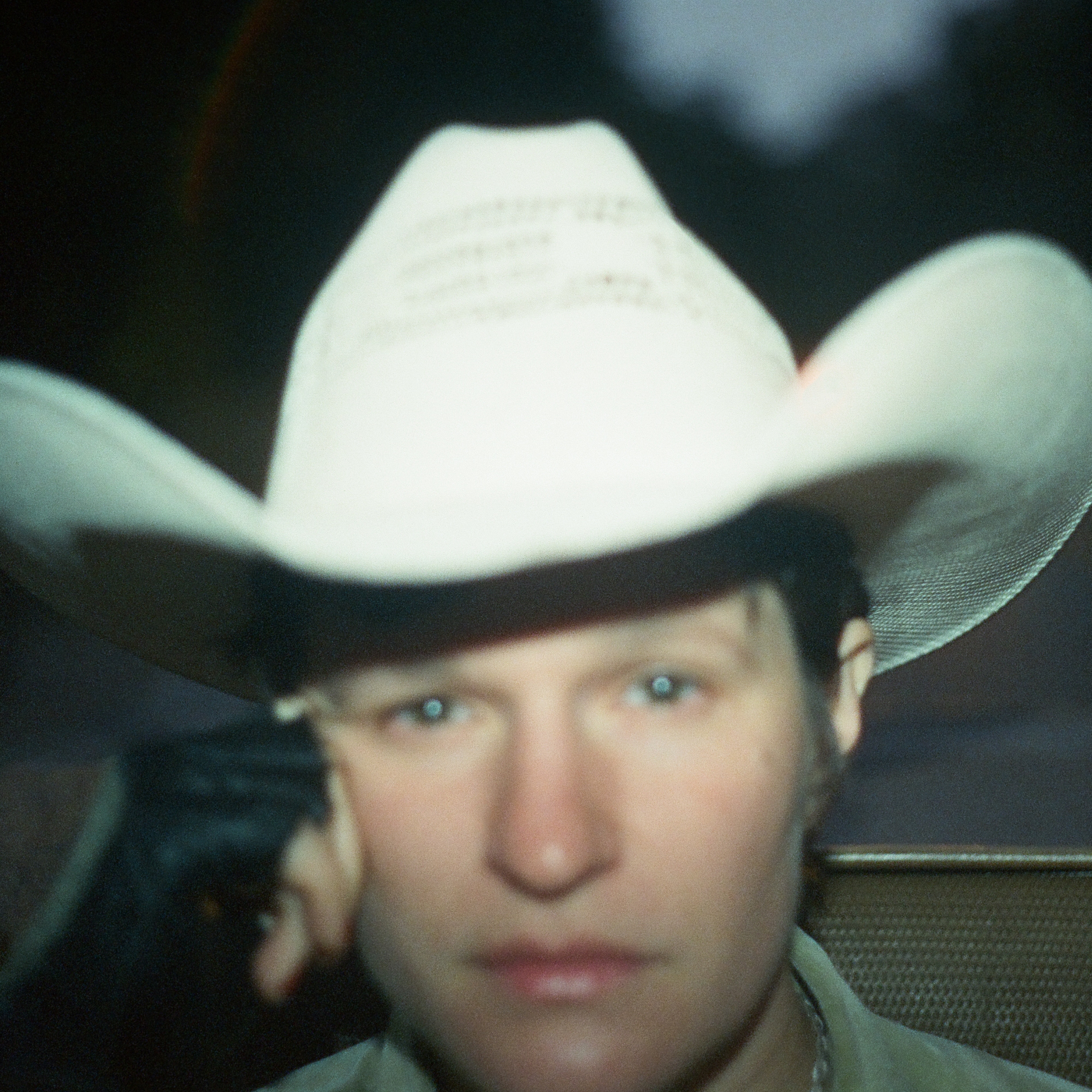 Out-of-focus portrait of woman wearing white cowboy hat with fingerless leather glove to her right temple