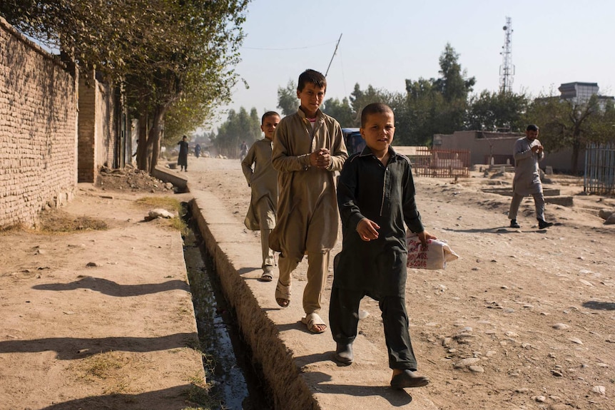 Three Afghanistan children walk down a dirt road.