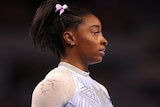 a head-and-shoulders image of gymnast simone biles with a bejewelled goat on the shoulder of her leotard