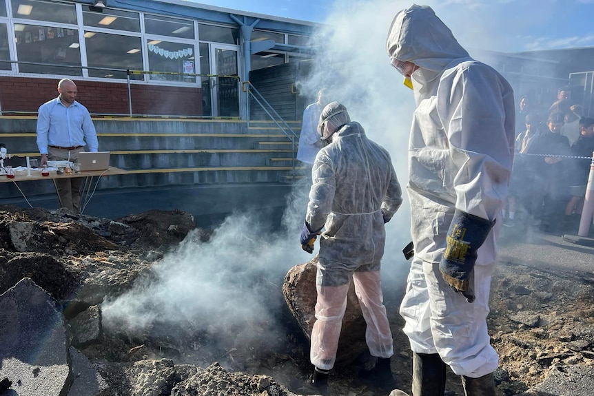 People in hazmat suits at a smoking hole.