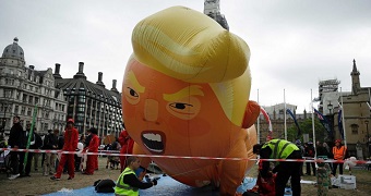 People inflate a giant balloon, shaped and designed to resemble Donald Trump in a nappy and with an angry look on his face.