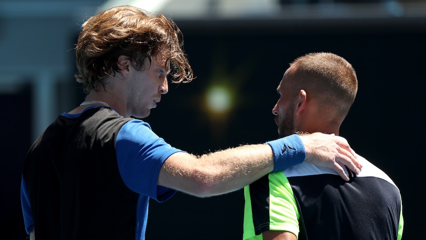 Two male tennis players embrace at the net at the Australian Open.
