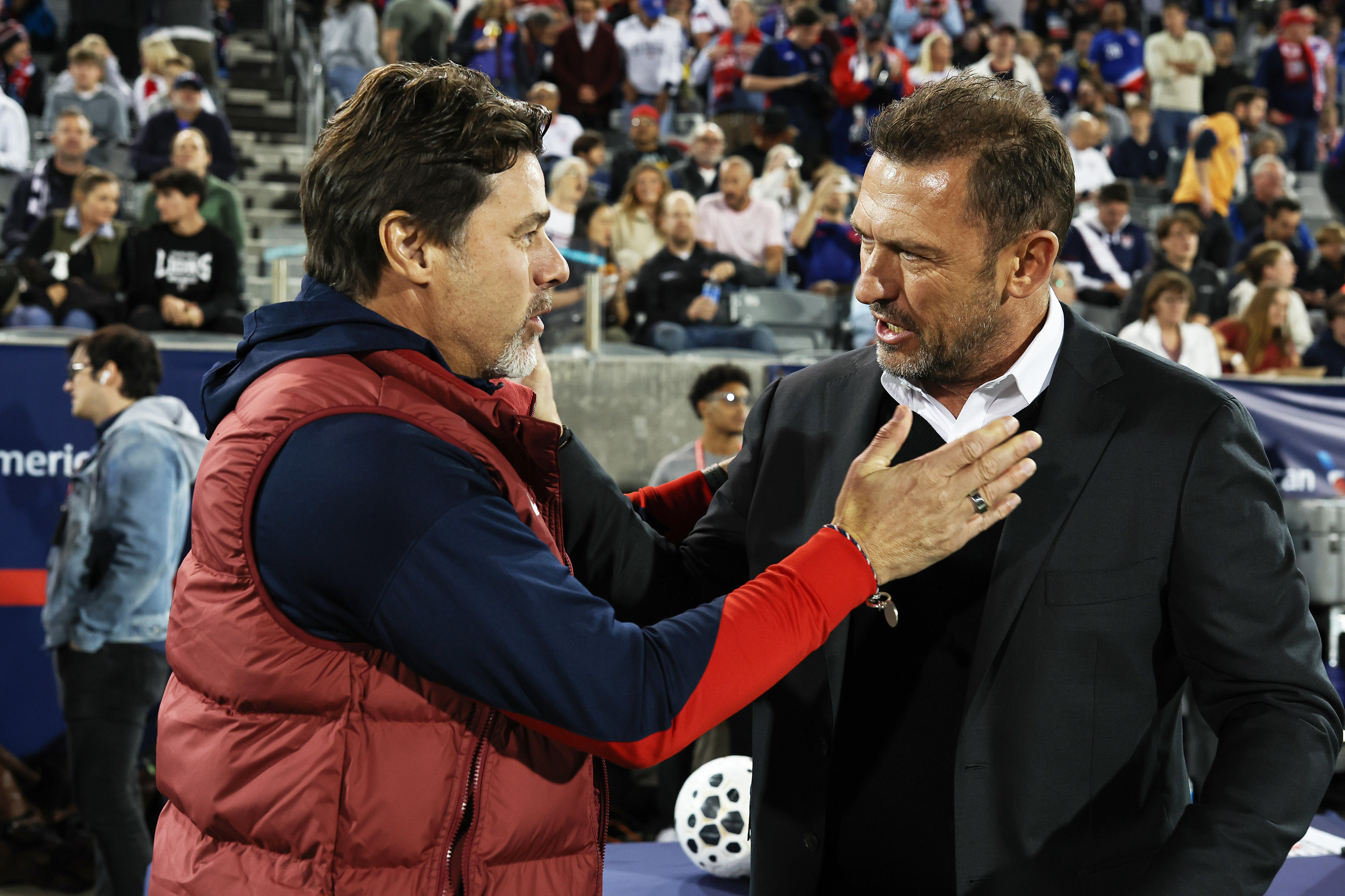 Two coaches speak to each other on the sidelines of a football match.
