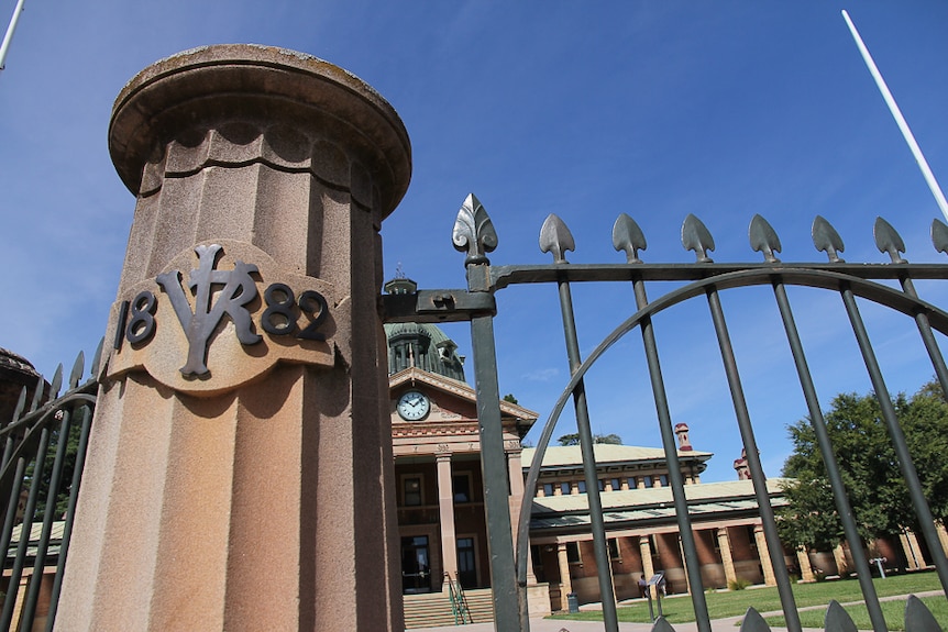 A column with 1882 on it and a gate with a colonial style courthouse in the background