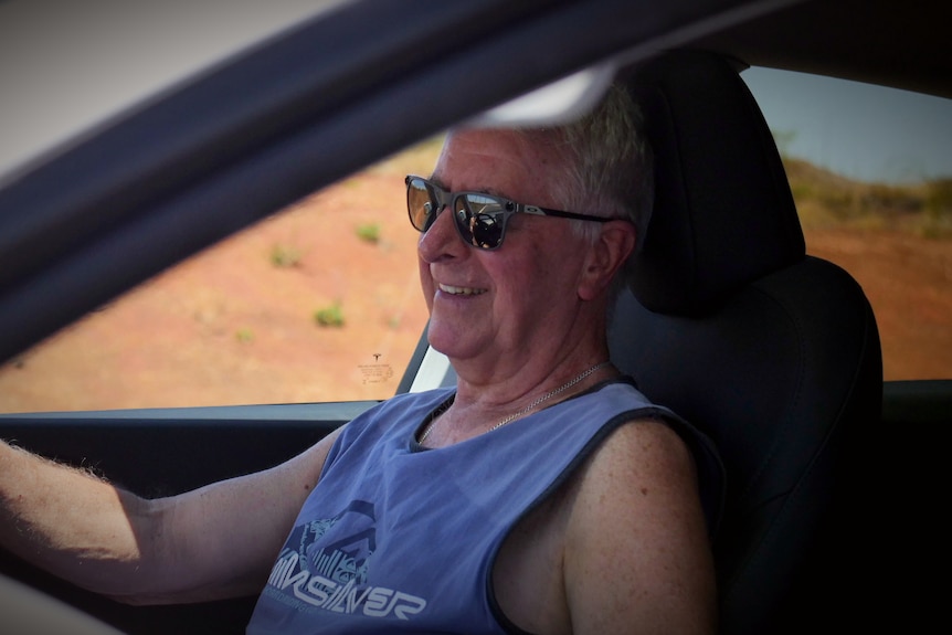 White man sitting inside car with red dirt in back