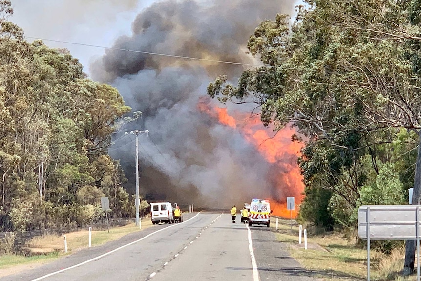 Big smoke flume and flames block a road.