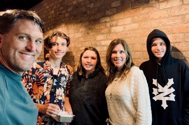 Jennifer Clayburn poses for a photo with her family in front of a brick background.