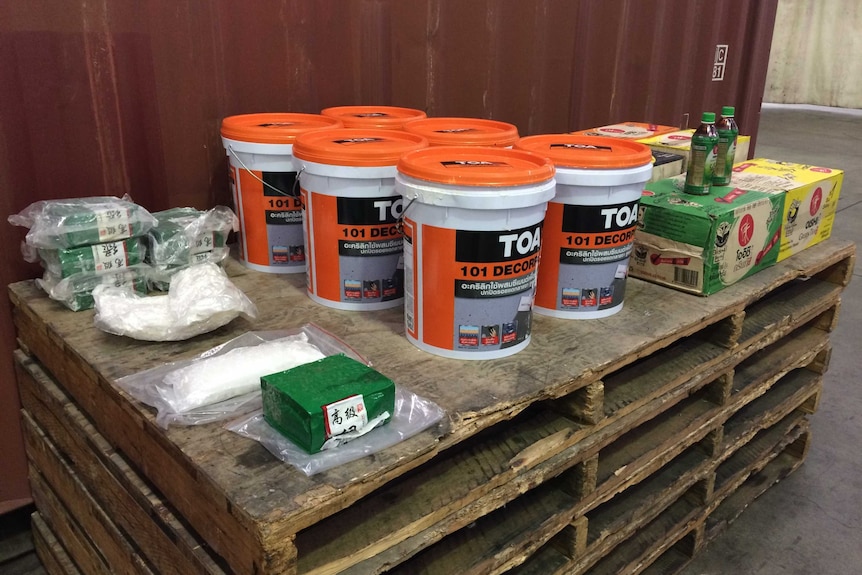 Bags of methamphetamine, buckets of plaster and green tea bottles sitting on a crate next to a shipping container.