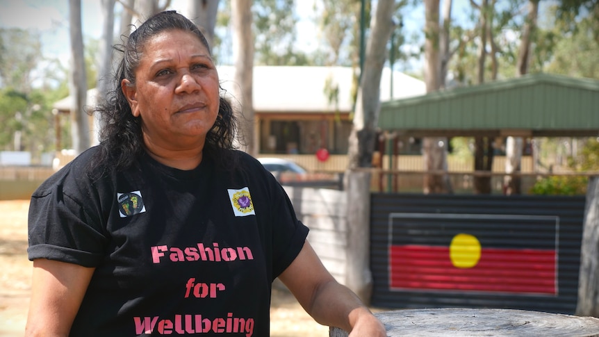 A woman leans her arm on a tree stump in front of a painting of the Aboriginal flag.